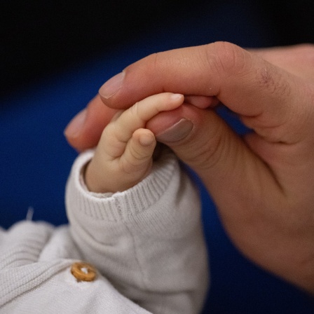 Ein Vater berührt während eines Infant Handling Kurses die Hand seines Kindes.