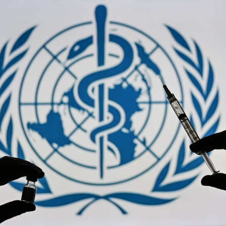 Eine Person hält eine medizinische Spritze und ein Impfstofffläschchen vor das Logo der Weltgesundheitsorganistaion WHO