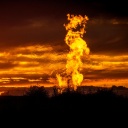 Eine Flamme schlägt vor glutrotem Abendhimmel auf einem Erdgasfeld in die Luft.