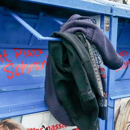 Am Einwurf eines Altkleidercontainers hängen zwei Kleidungsstücke.