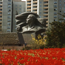 Das Ernst Thälmann Denkmal vor der Plattenbau-Kulisse in Berlin-Prenzlauer Berg. Im Vordergrund rote Blumen, im Hintergrund die Plattenbauten.
