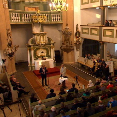 Menschen stehen und sitzen in einer Kirche.