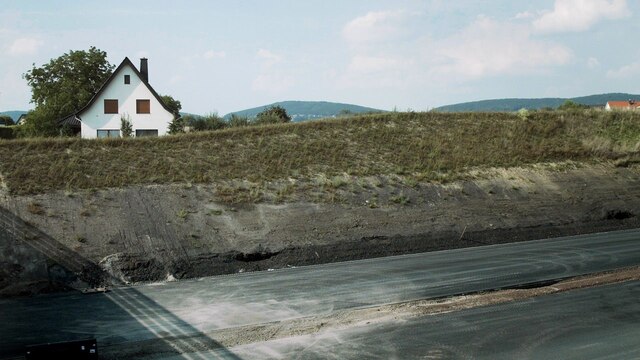 Ein Haus hinter einem Erdwall, davor eine Autobahnbaustelle