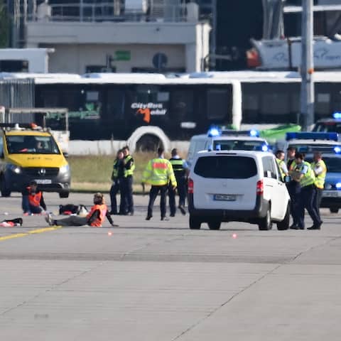 Klima-Aktivisten in orangen Warnwesten und Polizeibeamte auf einer Landebahn am Frankfurter Flughafen.