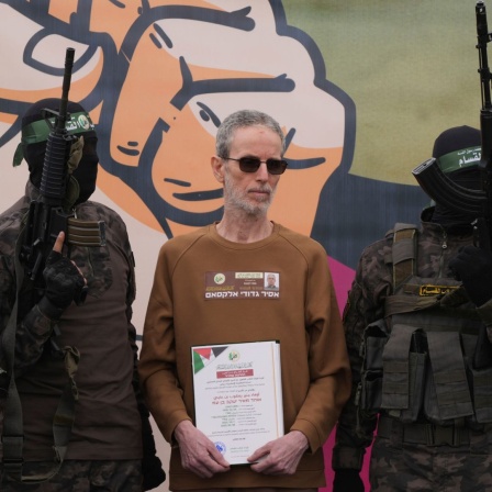 Der israelische Gefangene Ohad Ben Ami, der seit dem 7. Oktober 2023 von der Hamas im Gazastreifen als Geisel gehalten wird, wird von Hamas-Kämpfern eskortiert, bevor er dem Roten Kreuz im zentralen Gazastreifen übergeben wird.