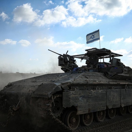 Ein israelisches Panzerfahrzeug mit Flagge wirbelt vor blauem Himmel Wüstensand auf.