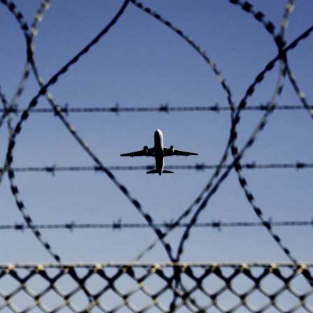 Ein Flugzeug fliegt hinter Stacheldraht.