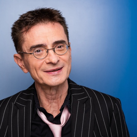 Der Kabarettist Mathias Richling ineeinem Nadelstreifenanzug vor einem blauen Hintergrund