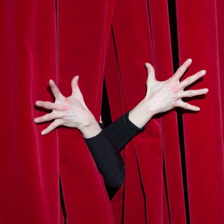 Hände auf einem roten Theatervorhang, Symbolbild