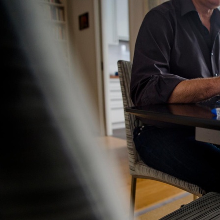 Ein Mann sitzt zuhause an einem Esstisch und arbeitet an einem Laptop 