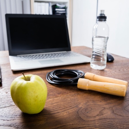 Nahaufnahme eines Tisches mit Laptop, Apfel, Wasser und Trainingsausrüstung (Bild: picture alliance / PantherMedia | Andriy Popov) 